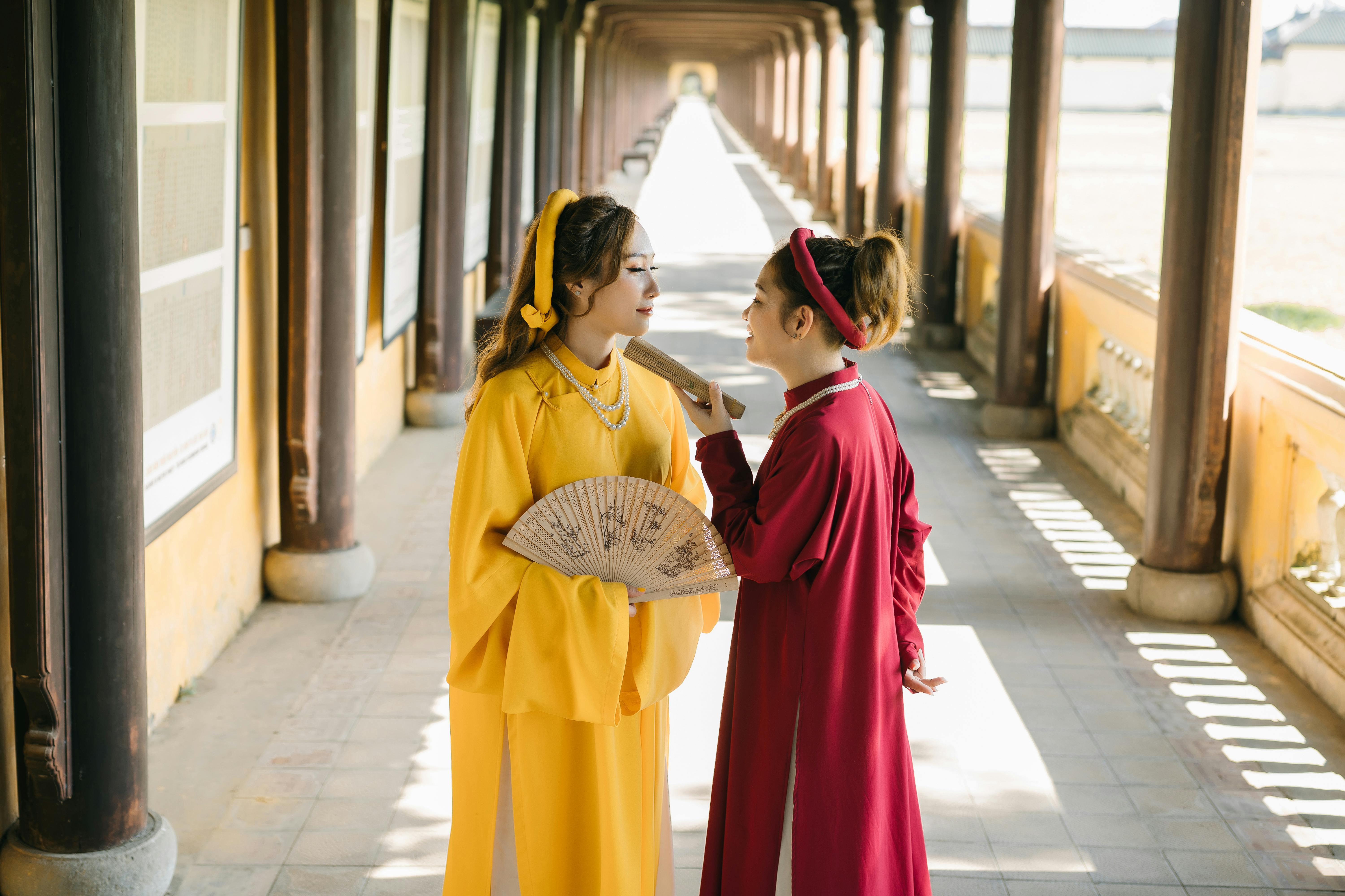 bisht robe - Two Asian women in traditional attire engage in a hallway, showcasing cultural elegance.