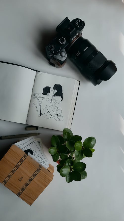 A Drawing of Couple on Notebook Beside a Camera