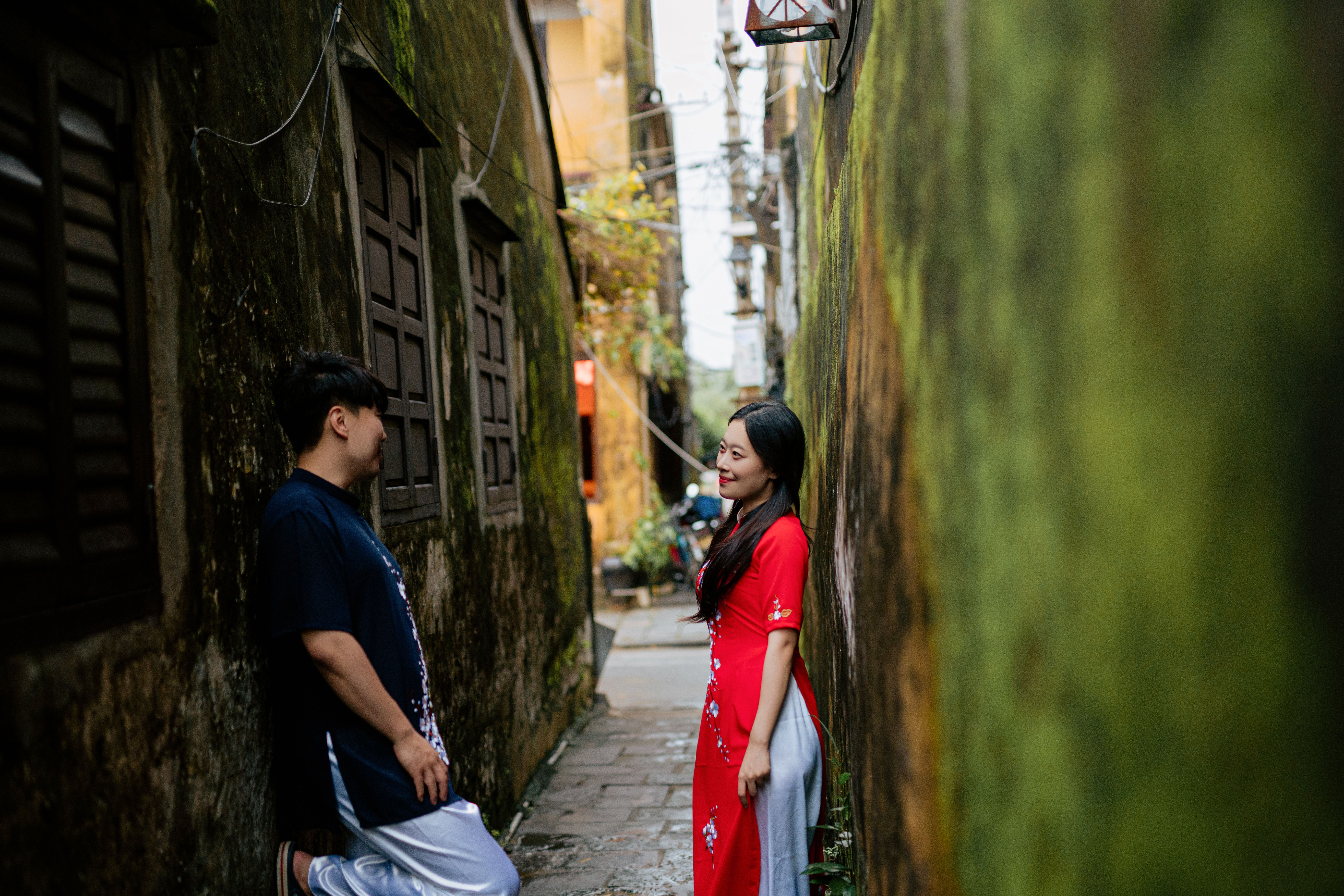 A couple in traditional attire shares a tender moment in a moss-covered alley.