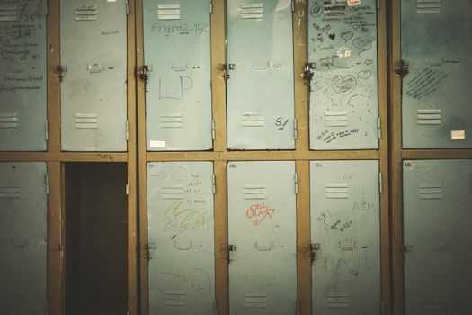 A row of vintage metal lockers with graffiti in an abandoned setting, offering rustic charm.