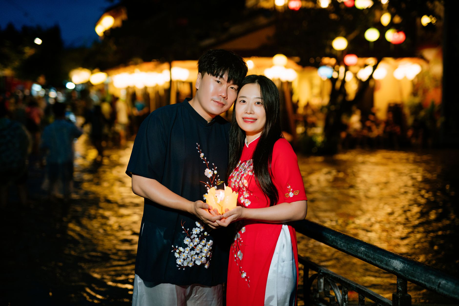 台中情侶牽手散步推薦:河畔公園步道8處浪漫地 An Asian couple standing by a riverside, embracing and holding a lantern at night.