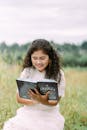 Girl Sitting on a Field Reading a Book and Smiling