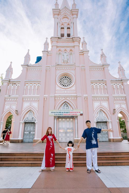 Free Family posing in traditional attire at a Gothic pink church on a sunny day. Stock Photo