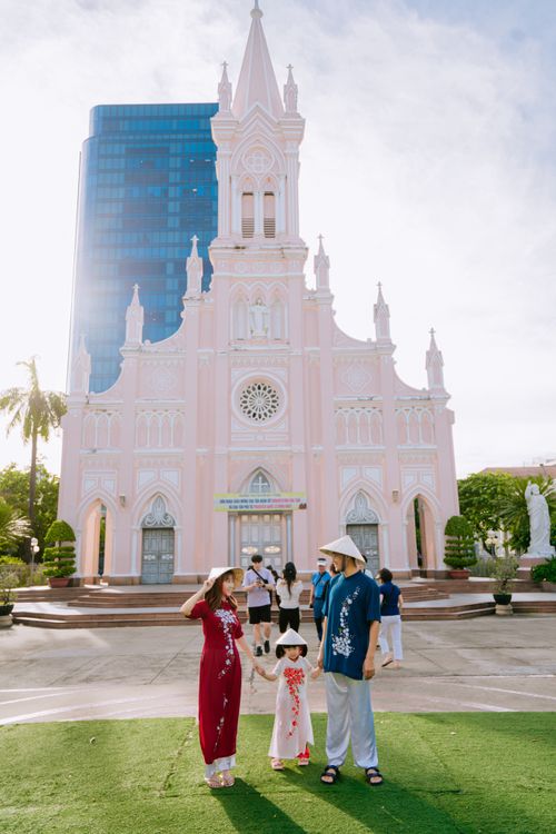 Free A family in traditional Vietnamese clothing stands before Da Nang Cathedral's pink facade. Stock Photo