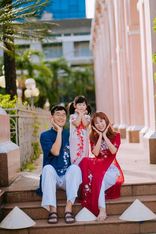 Free Smiling Asian family in traditional clothing sitting together outdoors, enjoying a sunny day. Stock Photo