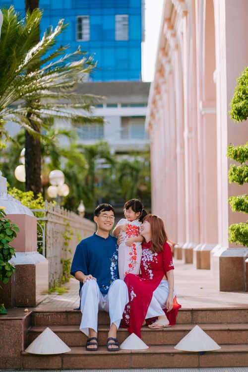 Free Smiling family of three sitting on stairs with colorful buildings in the background. Stock Photo