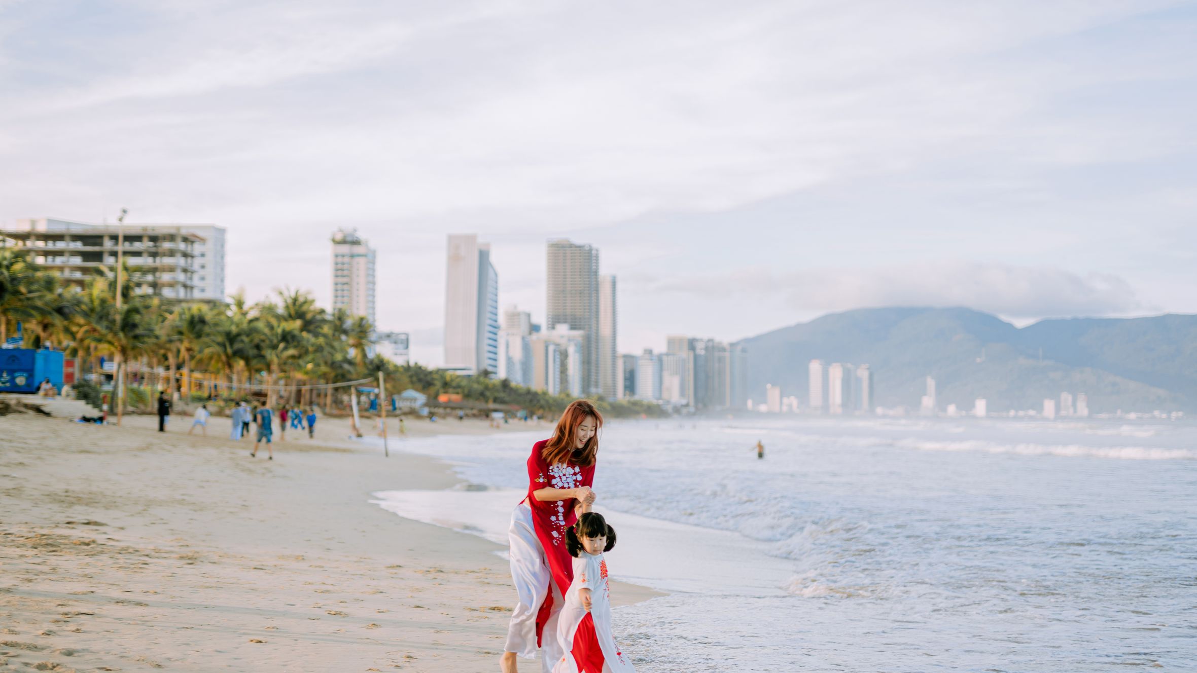A joyful mother and child walk hand in hand along a vibrant city beach, capturing a moment of happiness and bonding.