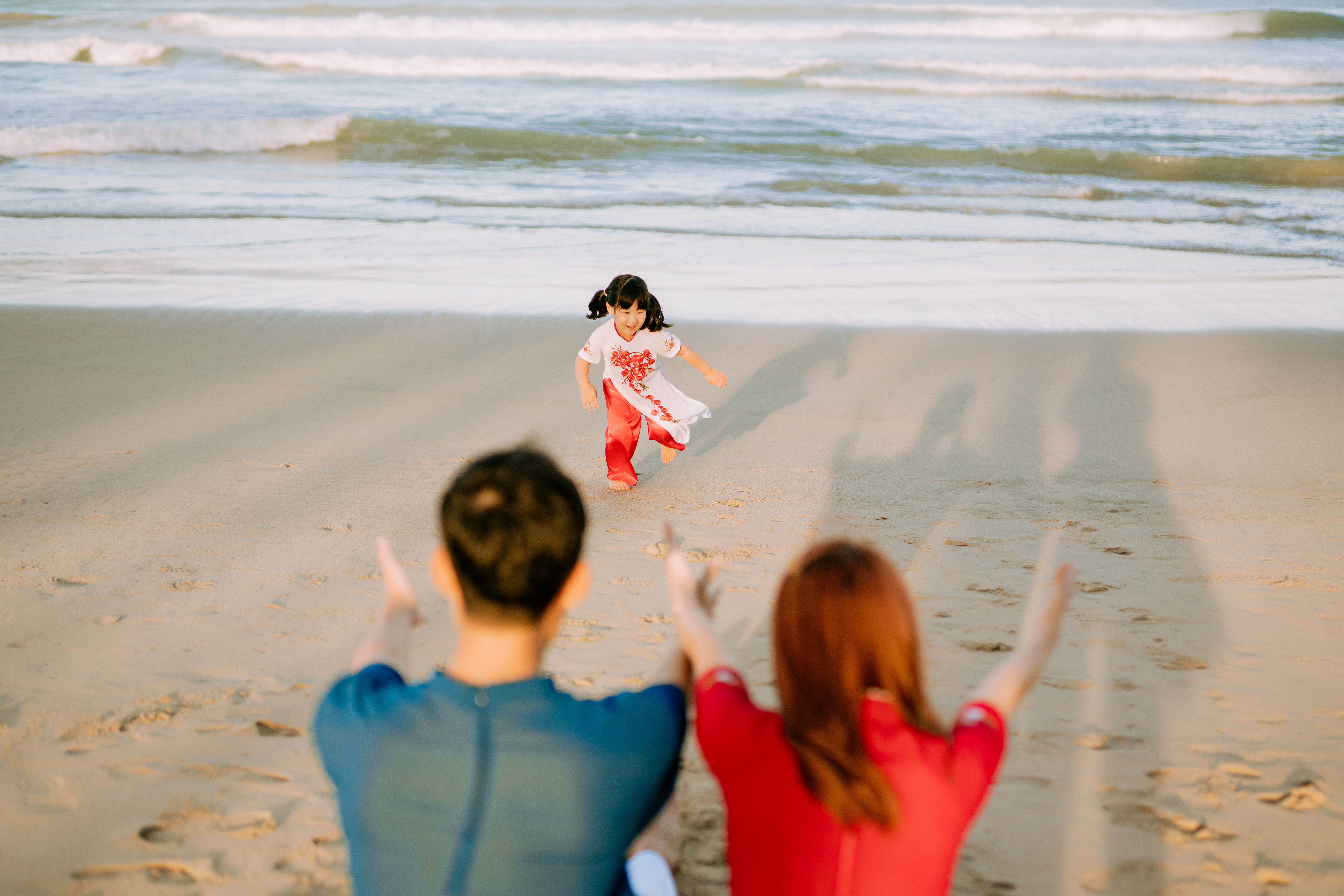 A young child runs joyfully towards parents on a sunny beach day.