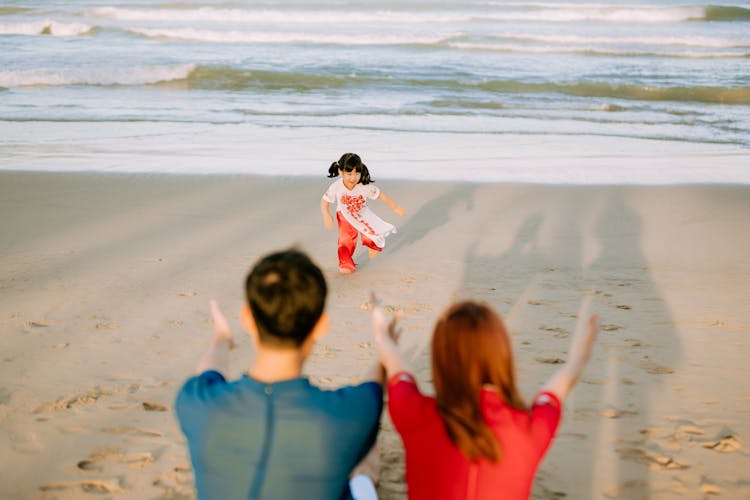 A Young Girl Running Towards Her Parents At The Beach