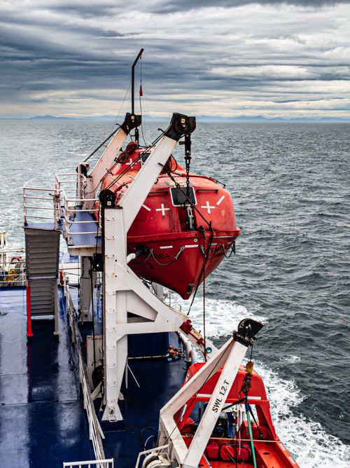 Free A bright red lifeboat hangs from an ocean vessel under a dramatic, cloudy sky. Stock Photo