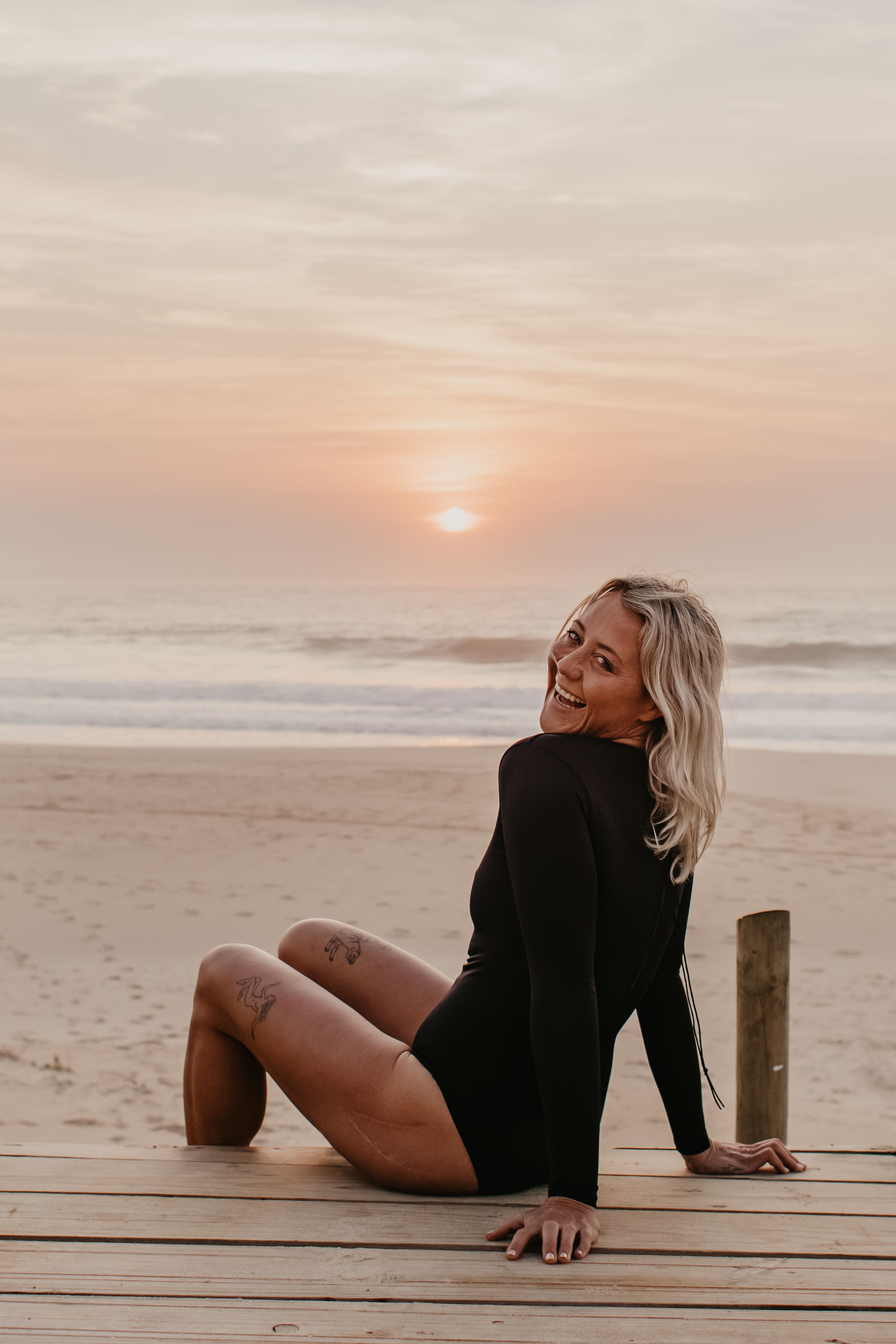 Smiling Woman In Black Wetsuit Sitting on Wooden Deck · Free Stock Photo