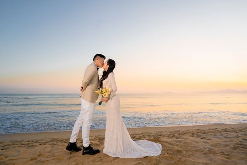 Free A couple shares a romantic kiss on the beach during their wedding at sunset. Stock Photo