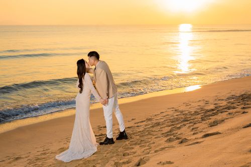 Free Bride and groom share a romantic kiss on the beach at sunset, enjoying an intimate wedding moment. Stock Photo