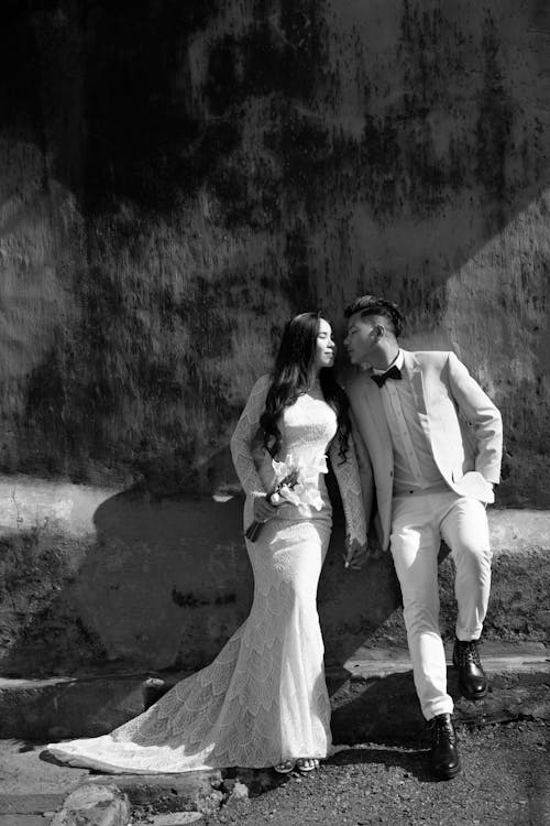 Grayscale Photo of Man and Woman Standing beside Concrete Wall