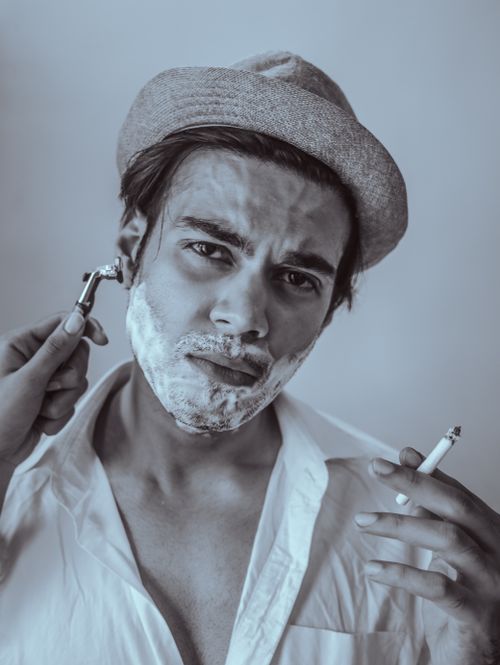 Free Artistic portrait of a man in a fedora being shaved while smoking, with a vintage vibe. Stock Photo