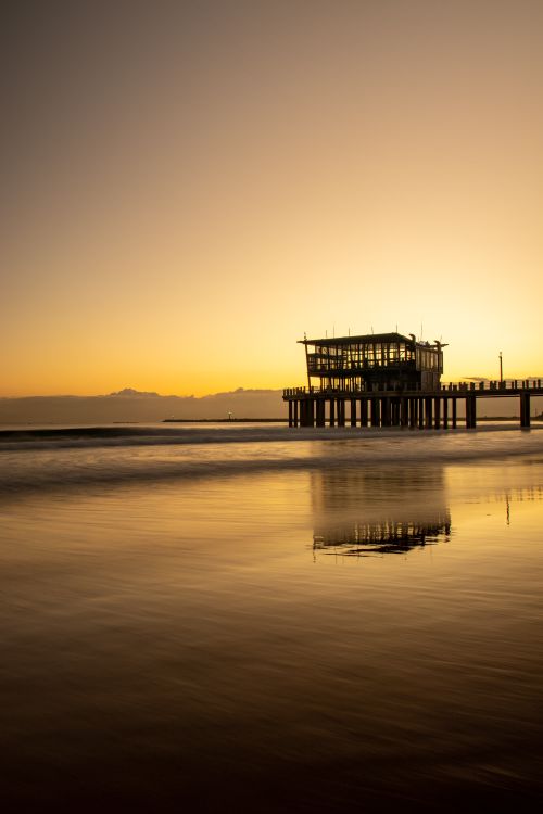 Free Breathtaking sunset view of Durban's pier reflecting over the calm ocean water. Stock Photo