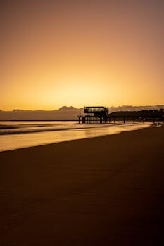 Peaceful sunrise view of the pier on Durban's coast with golden hues reflecting on the shore.