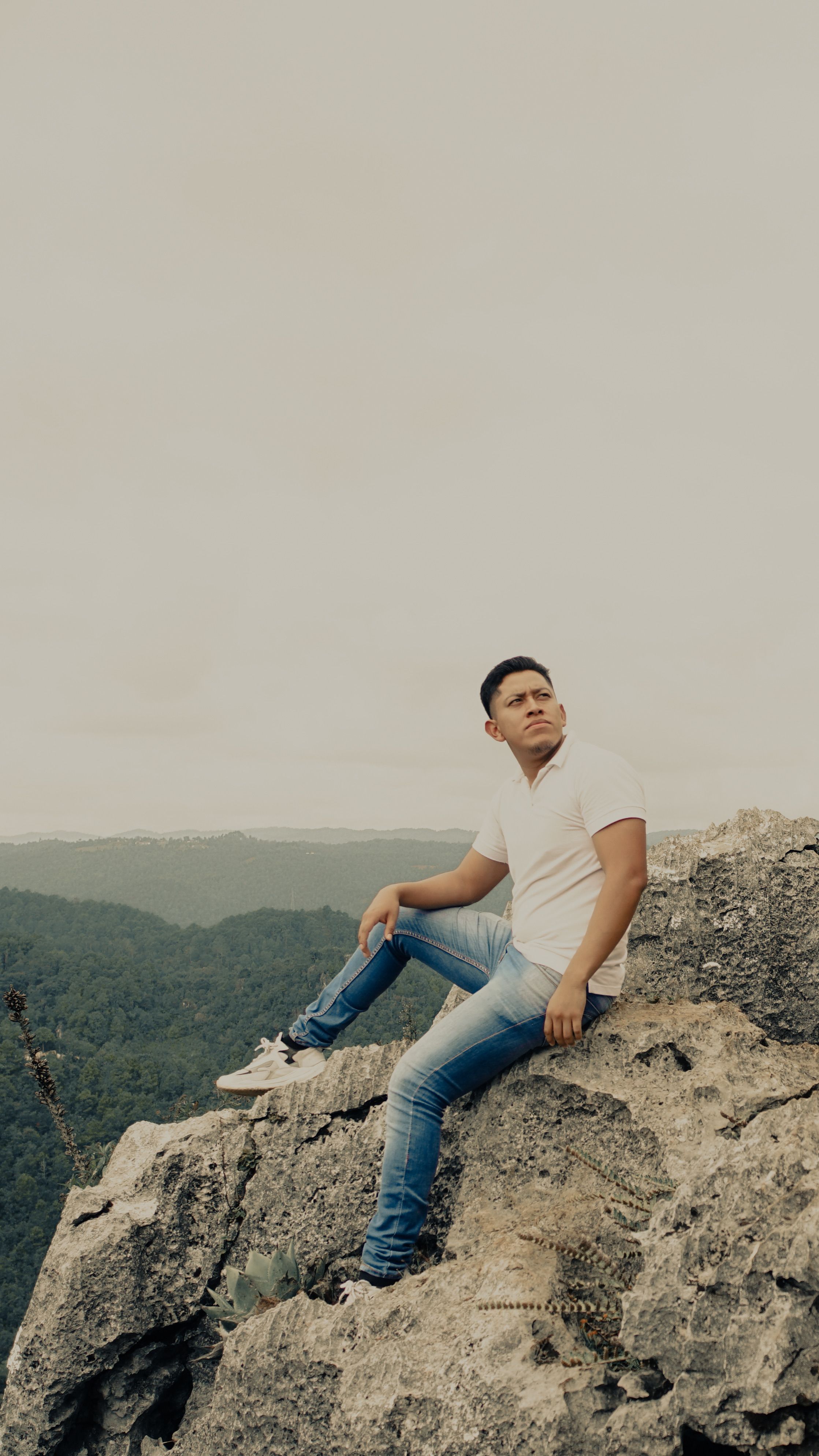 A man in casual attire sits on a rock gazing over a lush valley. Perfect for outdoor and adventure themes.