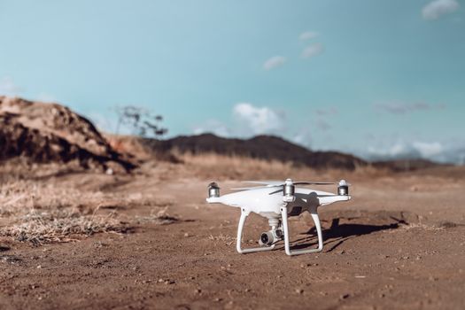 White drone ready for takeoff on a rugged desert landscape under a clear blue sky.