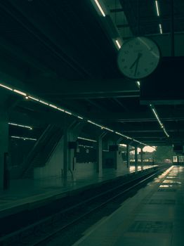 A quiet, dimly lit train platform with an illuminated clock showing time at a modern station.