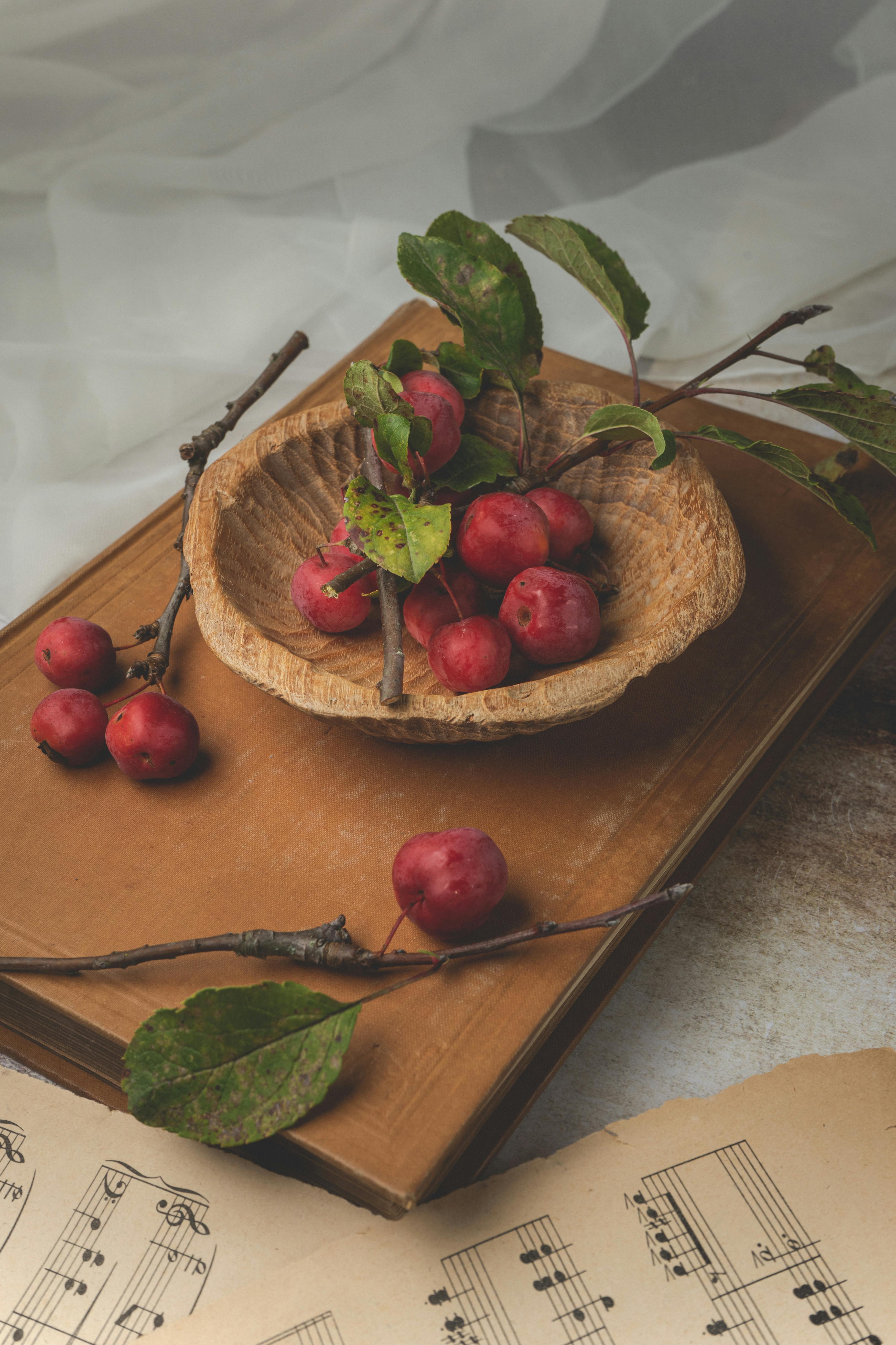 Vintage setup with red apples in a bowl on wooden surface, surrounded by sheet music and leaves.