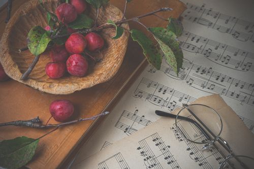 Free Rustic still life featuring a bowl of red plums, eyeglasses, and sheet music. Stock Photo