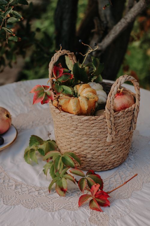 Free A rustic basket filled with small pumpkins and autumn leaves on a lace tablecloth outdoors. Stock Photo