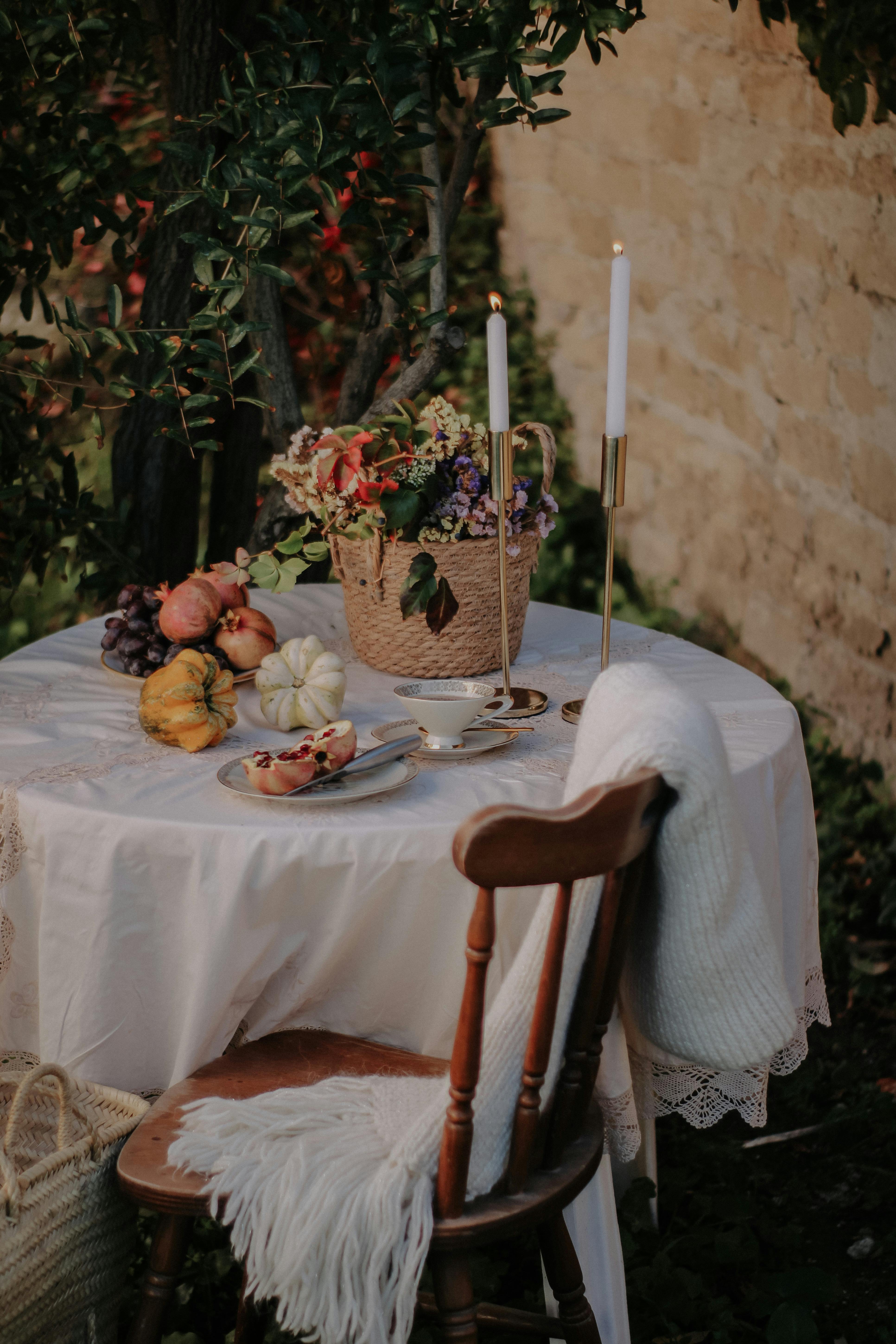 Cozy outdoor table setup with candles, flowers, and autumn vegetables on a rustic chair.