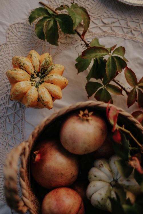 Free A cozy autumn-themed flat lay of a basket filled with pomegranates and gourds on a lacy tablecloth. Stock Photo