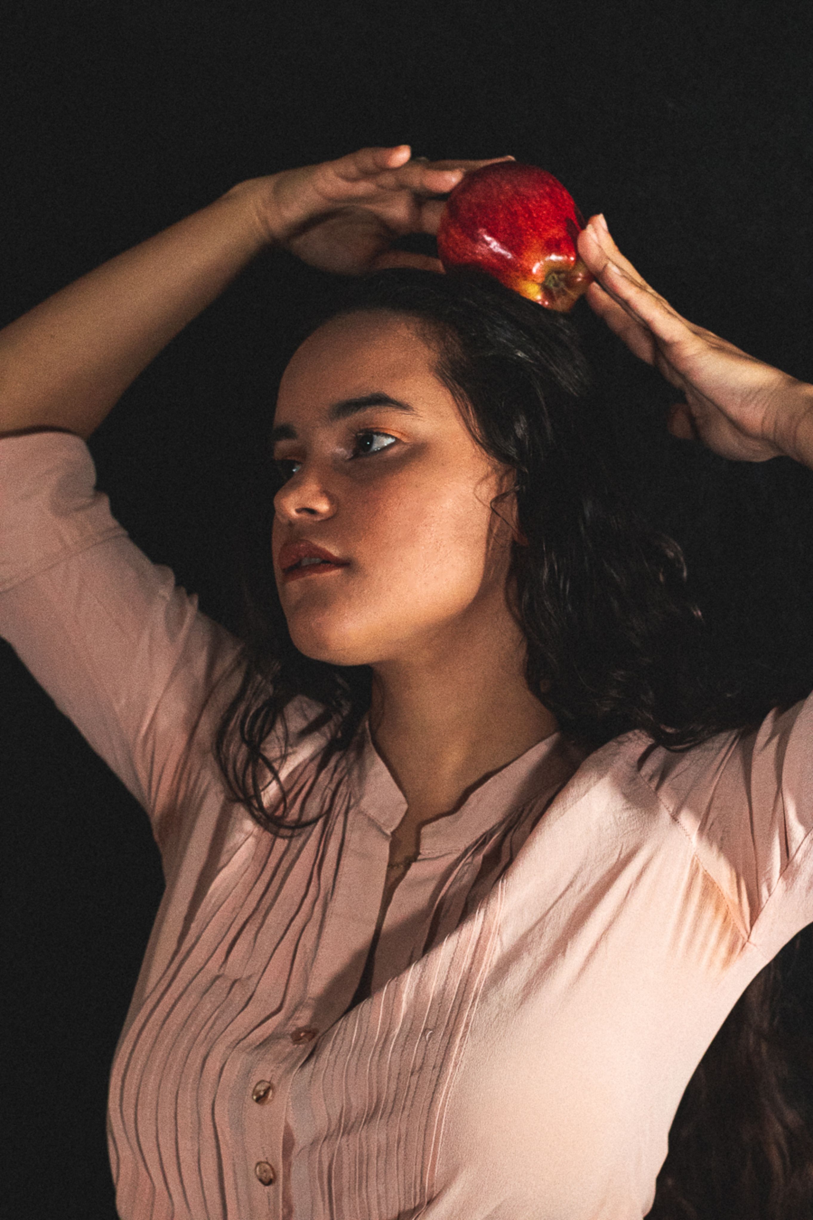 Close-up of a young woman with black hair, holding a red apple against a dark background.