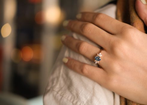 Close-up of a hand wearing a sapphire engagement ring with diamonds.