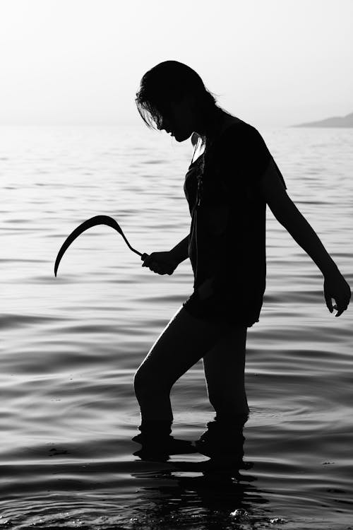 Person Standing in Body of Water While Holding Sickle