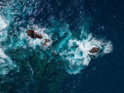 Free Dynamic aerial shot capturing waves crashing onto rugged rocks in the deep blue sea. Stock Photo
