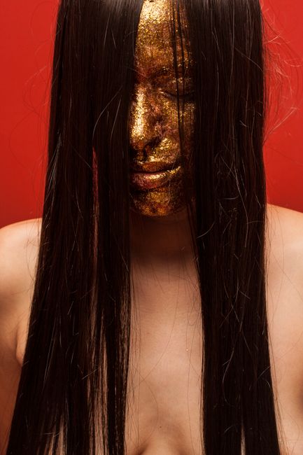 Artistic portrait of a woman with a golden mask and dark hair on a red background.
