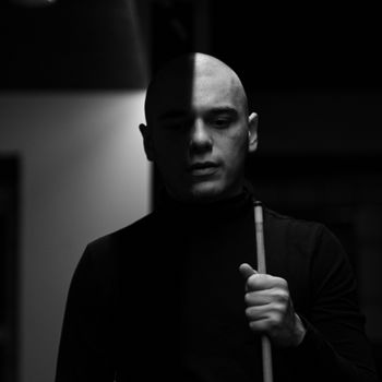 Moody black and white portrait of a concentrated billiards player holding a cue stick.