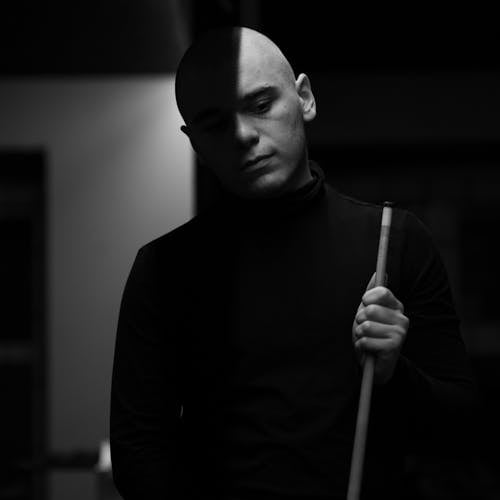 A Grayscale Photo of a Man in Turtleneck Sweater Holding a Cue Stick
