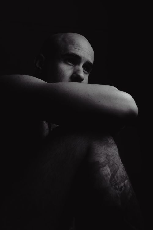 Free A dramatic black and white portrait of a bald man sitting in shadow, conveying introspection and emotion. Stock Photo