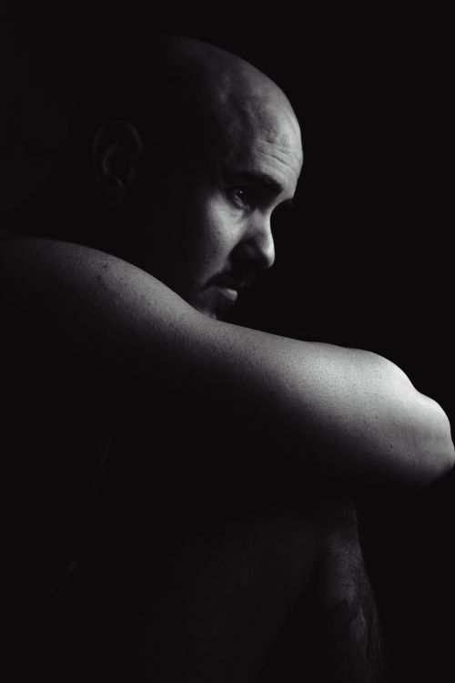Free A dramatic black and white portrait capturing a bald man in a thoughtful pose with deep shadows. Stock Photo