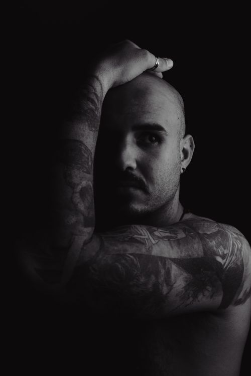 Free Artistic black and white portrait of a bald man with tattoos, partially obscured face and moody lighting. Stock Photo