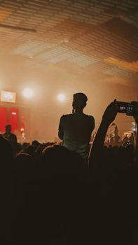 Silhouette of a man enjoying an indoor concert with vibrant lighting and audience capturing the moment.