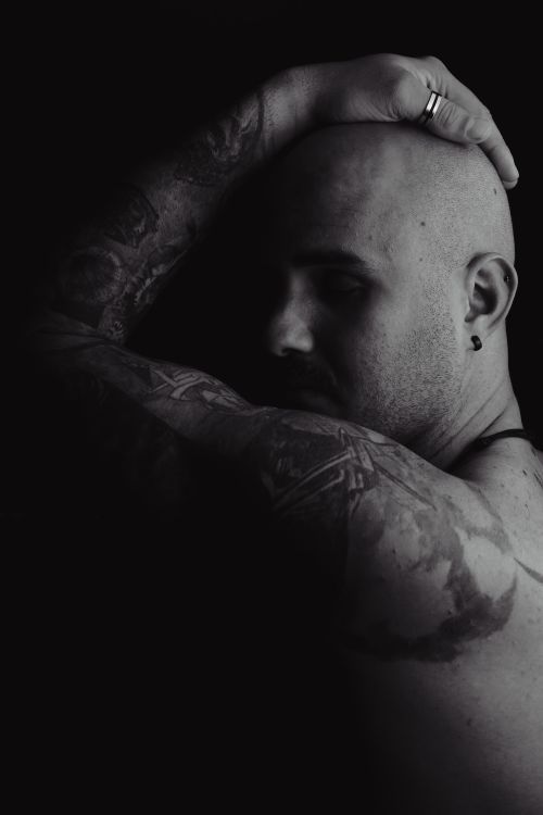 Free Moody black and white portrait of a bald, tattooed man with hand on head. Stock Photo