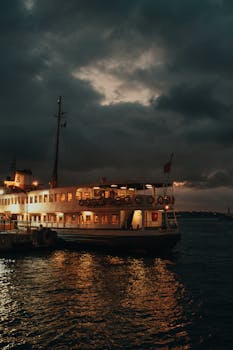 A serene and picturesque scene featuring an illuminated ferry docked at sunset with dramatic skies overhead.