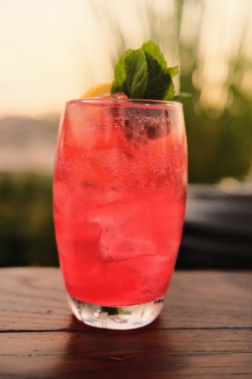 Free Close-up of a vibrant pink cocktail garnished with mint and lemon on a summer evening. Stock Photo