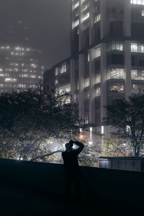Free Silhouette of a photographer capturing skyscrapers amidst night fog in a cityscape. Stock Photo