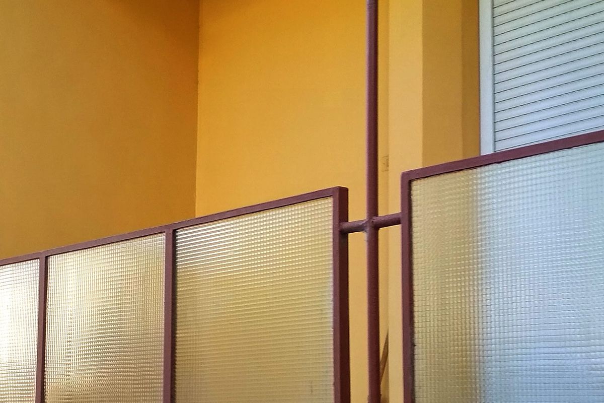Balcon minimalist cu balustradă de sticlă, pe o fațadă portocalie luminată de soare