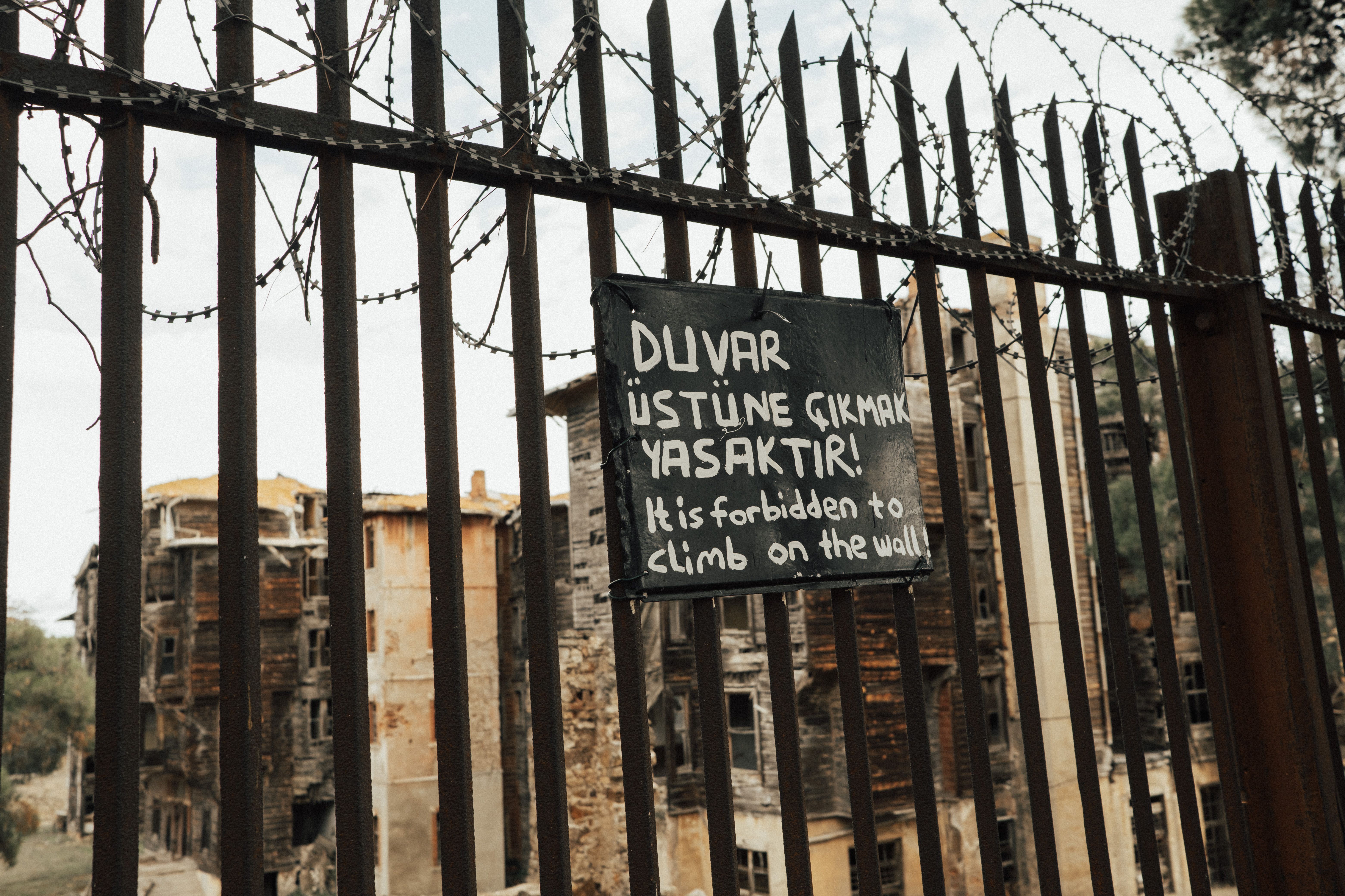 Barbed wire fence in front of an abandoned building with a warning sign prohibiting climbing.