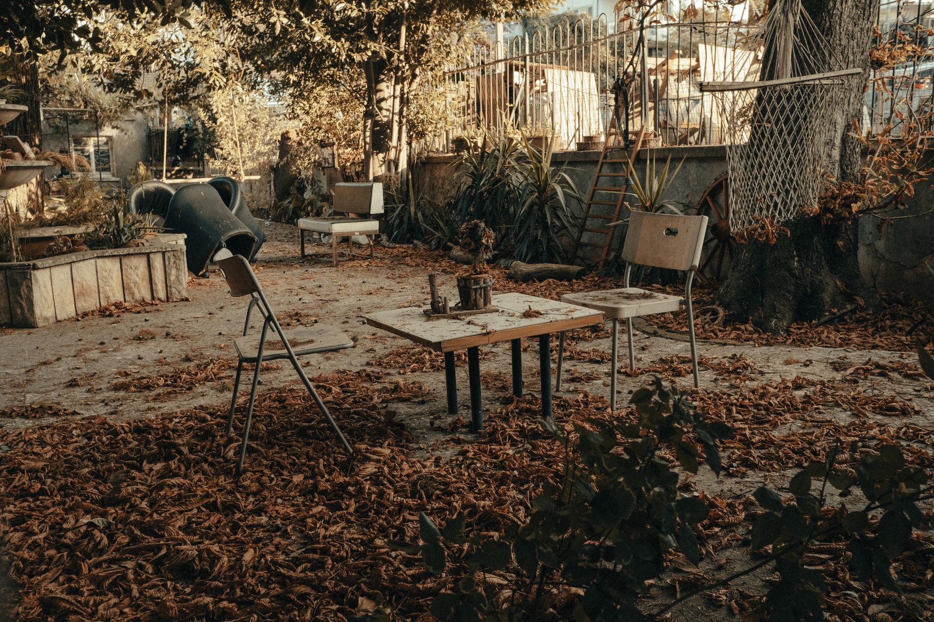 Weathered chairs and table in an abandoned garden setting, surrounded by fall leaves.
