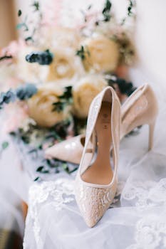 Close-up of elegant bridal high heels on lace with floral bouquet in soft focus.