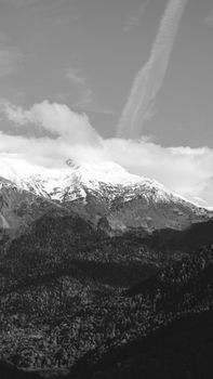 Black and white photo of snow-capped mountains with clouds and a clear sky.