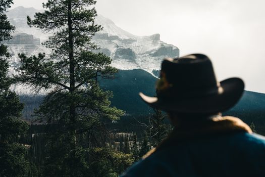 A cowboy in a hat gazes at snow-capped mountains in Jasper, Canada. Serene and majestic sight.